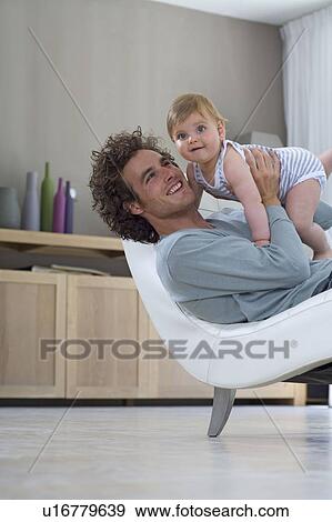 Stock Photo - Happy father holds up baby at home. Fotosearch