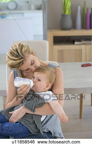 Mother kisses and bottle feeds baby View Large Photo Image Stock Photograph - Mother kisses and bottle feeds baby. Fotosearch
