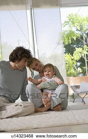 Stock Photo - Parents laugh with baby on floor. Fotosearch