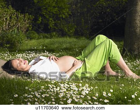 Stock Image - Pregnant woman in the garden, smiling. Fotosearch