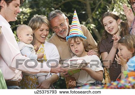 Stock Image - Young boy blowing out candles at party. Fotosearch