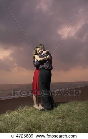 Stock Photo - Couple hugging by a beach at sunset.. Fotosearch
