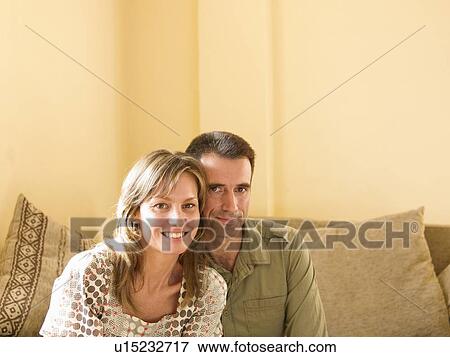 Stock Photo - Couple sitting on sofa at home, smiling, portrait. Fotosearch