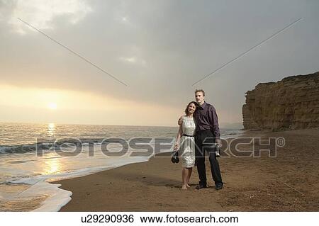 Stock Photograph - Couple standing on beach at sunset.. Fotosearch