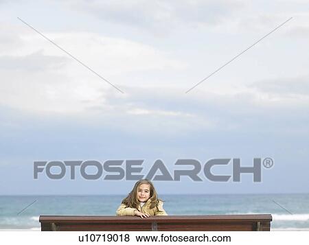 Girl (6-8) sitting on bench by sea, smiling, portrait View Large Photo Image Stock Photo - Girl (6-8) sitting on bench by sea, smiling, portrait. Fotosearch