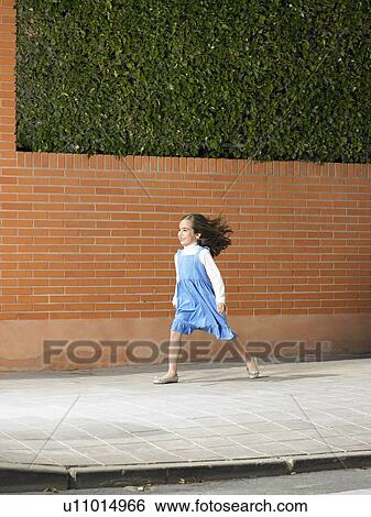 Stock Photograph - Little girl (5-7) running down pavement against the wind, Alicante, Spain,. Fotosearch