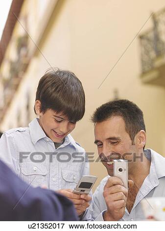 Stock Photo - Man holding camera phone, son (8-10) sending text message, smiling. Fotosearch