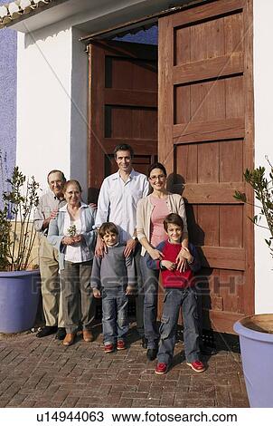 Stock Image - Multi-generational family standing at front door, smiling, portrait. Fotosearch