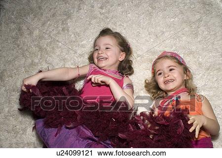Stock Image - Two girls (2-4) dressed for a party, lying on rug.. Fotosearch
