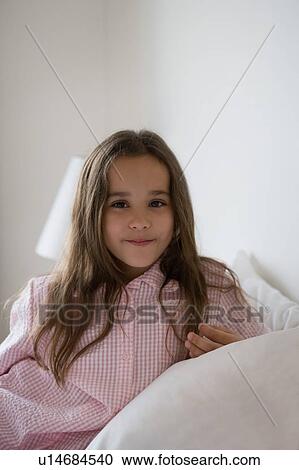 Stock Image - Young girl sitting on a bed portrait.. Fotosearch