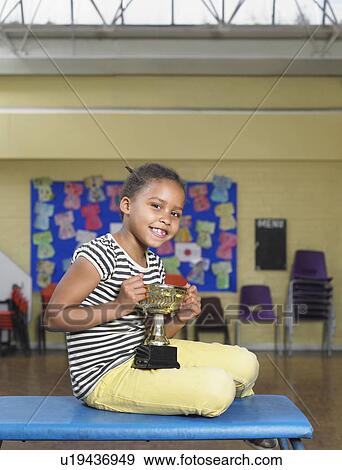 Stock Photo - Young girl with trophy in school hall. Fotosearch