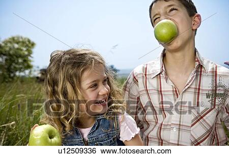 Boy holding apple in teeth with girl View Large Photo Image Stock Photograph - Boy holding apple in teeth with girl. Fotosearch