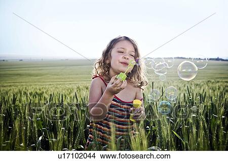 Picture - Girl blowing bubbles in wheat field. Fotosearch