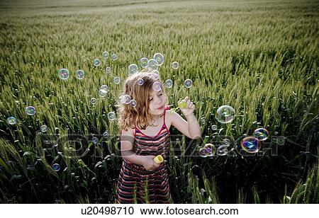 Stock Image - Girl blowing bubbles in wheat field. Fotosearch