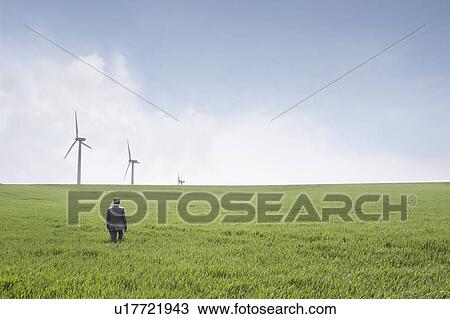 Stock Image - Man walking towards wind turbines. Fotosearch