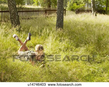 Stock Image - Woman lying in the grass reading.. Fotosearch