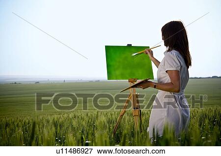 Stock Photo - Woman painting in wheat-field, rear. Fotosearch