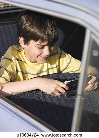 Picture - Boy (8-10) playing portable video game in backseat of car. Fotosearch