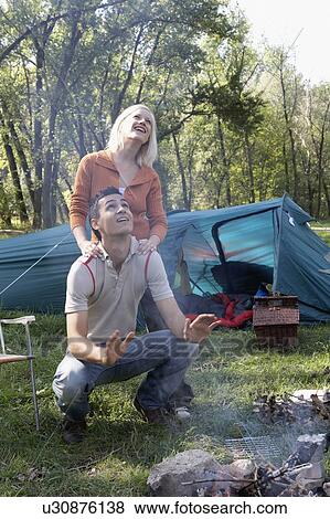 Couple at campsite looking up at smoke from the fire pit smiling. View Large Photo Image Stock Photo - Couple at campsite looking up at smoke from the fire pit smiling.. Fotosearch