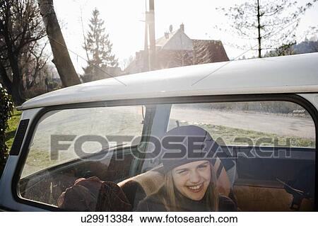 Girl (10-12) sitting in back of car, smiling, view through window View Large Photo Image Picture - Girl (10-12) sitting in back of car, smiling, view through window. Fotosearch