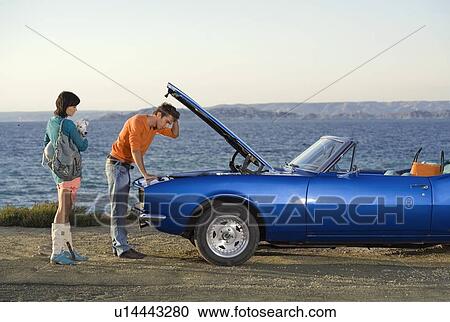 Stock Image - Man and woman man looking under car.. Fotosearch