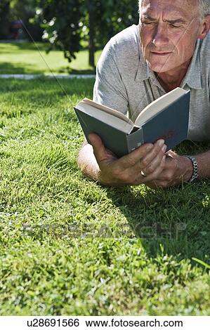 Stock Photograph - Man lying on grass reading. Fotosearch