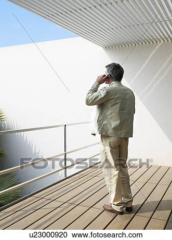 Man standing on balcony using mobile phone, rear view View Large Photo Image Stock Image - Man standing on balcony using mobile phone, rear view. Fotosearch