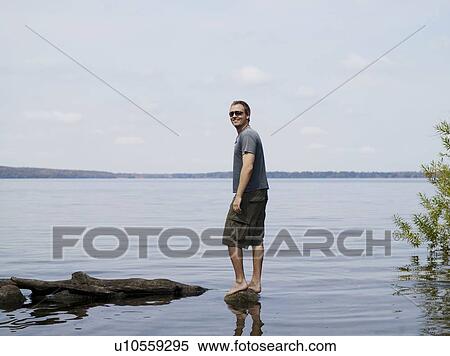 Stock Photography - Man standing on rock in shallow water. Fotosearch