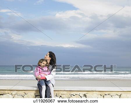 Mother cuddling daughter (6-8) on wall next to beach. Alicante, Spain. View Large Photo Image Stock Photo - Mother cuddling daughter (6-8) on wall next to beach. Alicante, Spain.. Fotosearch
