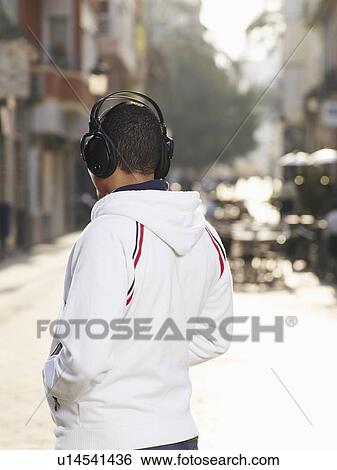 Young man standing in street wearing headphones, rear view View Large Photo Image Stock Photograph - Young man standing in street wearing headphones, rear view. Fotosearch