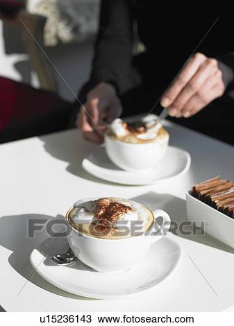 Cappuccino on table, woman stirring cup in background View Large Photo Image Stock Image - Cappuccino on table, woman stirring cup in background. Fotosearch