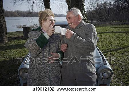 Senior couple standing by car toasting each other with cups, smiling View Large Photo Image Stock Image - Senior couple standing by car toasting each other with cups, smiling. Fotosearch