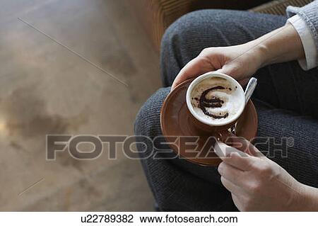 Stock Image - Woman holding cappuccino with euro motif. Fotosearch