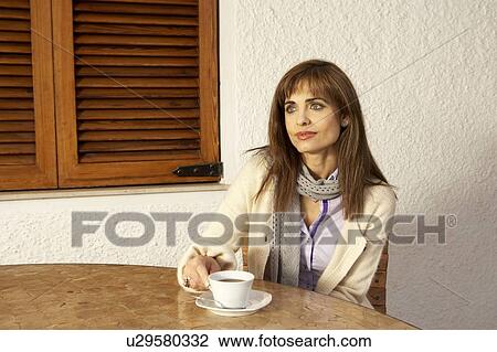 Woman sitting at table holding Coffeee cup View Large Photo Image Stock Image - Woman sitting at table holding Coffeee cup. Fotosearch