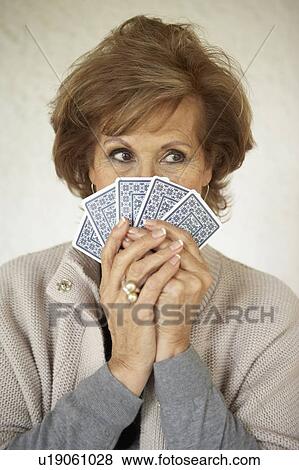 Stock Photo - Senior woman holding playing cards over face, close-up. Fotosearch