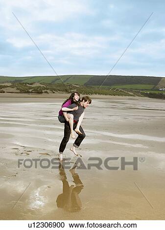 Man carrying woman piggy back on beach View Large Photo Image Stock Image - Man carrying woman piggy back on beach. Fotosearch