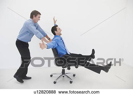 Stock Photo - Man pushes man in office chair. Fotosearch