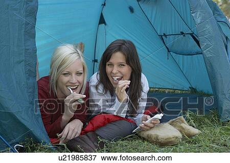 Stock Photo - Two women at campsite brushing teeth in tent and smiling.. Fotosearch