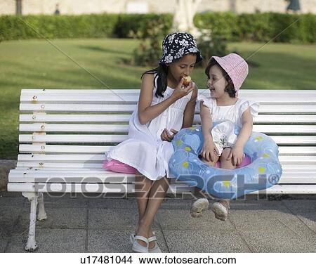 Two young girls sitting on bench View Large Photo Image Picture - Two young girls sitting on bench. Fotosearch