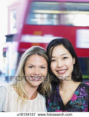 Stock Photo - Two young women in street, smiling, portrait, close-up. Fotosearch