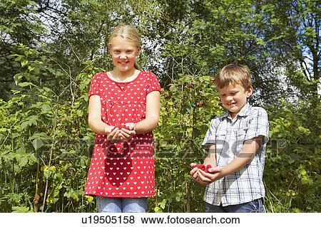 Stock Photo - Young boy and young girl standing outdoors holding fresh raspberries.. Fotosearch