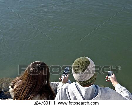 Young couple looking at mobiles View Large Photo Image Stock Image - Young couple looking at mobiles. Fotosearch