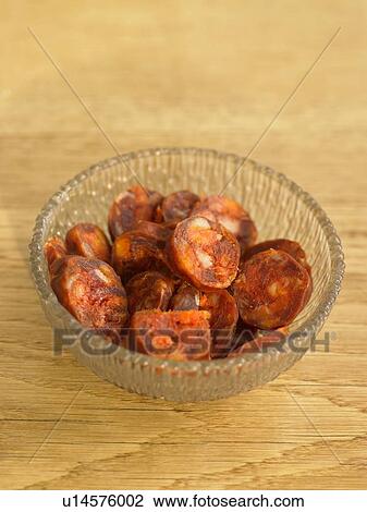 Stock Image - Bowl of chorizo on wooden table, close-up. Fotosearch