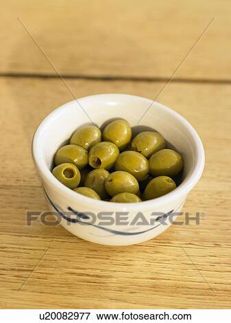Stock Photo - Bowl of green olives on wooden table, close-up. Fotosearch
