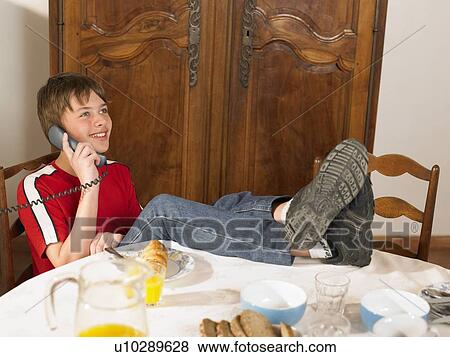 Stock Photo - Boy (11-13) talking on phone at breakfast table. Fotosearch
