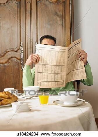 Picture - Man sitting at breakfast table reading newspaper. Fotosearch
