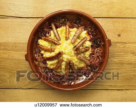Stock Photo - Sausage and mash with caramelized onions in bowl standing on wooden table. Fotosearch