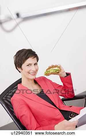 Stock Image - Woman eating sandwich at her office . Fotosearch