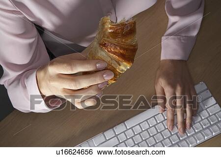 Stock Photograph - Woman's hands typing and holding a croissant.. Fotosearch