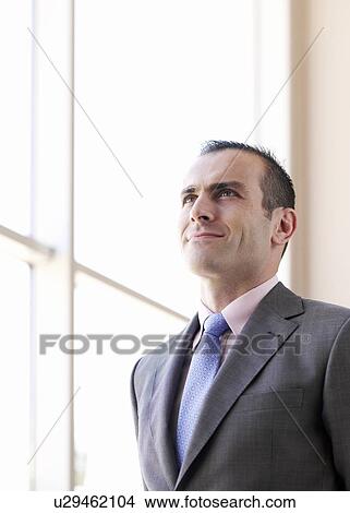 Picture - Businessman standing by window, smiling, low angle view. Fotosearch